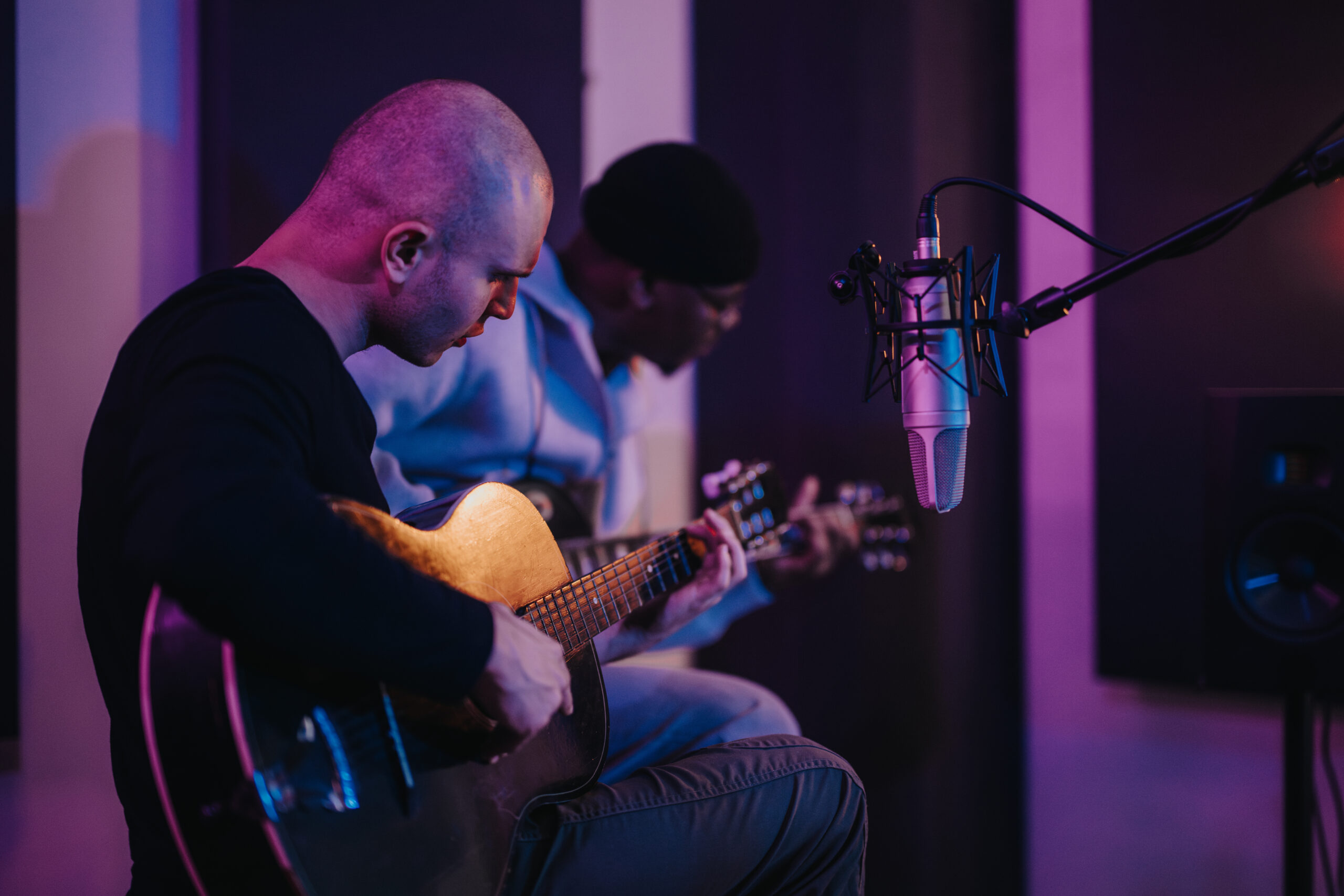 Musicians playing acoustic guitars in a recording studio with purple lighting