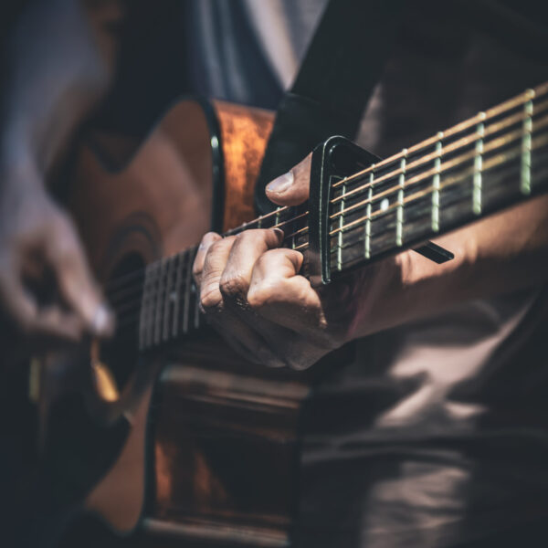 A man plays an acoustic guitar in the dark, close-up.