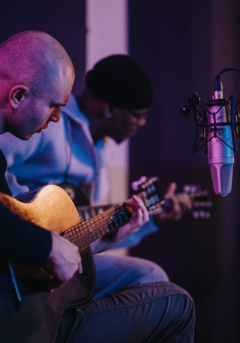 Musicians playing acoustic guitars in a recording studio with purple lighting