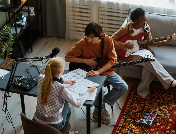 High angle view of young musicians writing songs together and playing musical instruments in studio